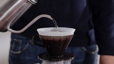 Coffee Drip Concept. Person Pouring Hot Water from Kettle into a Dripper. Making Pour Over Hot Coffee Drink in House. Zen and Cozy Living. Closeup shot