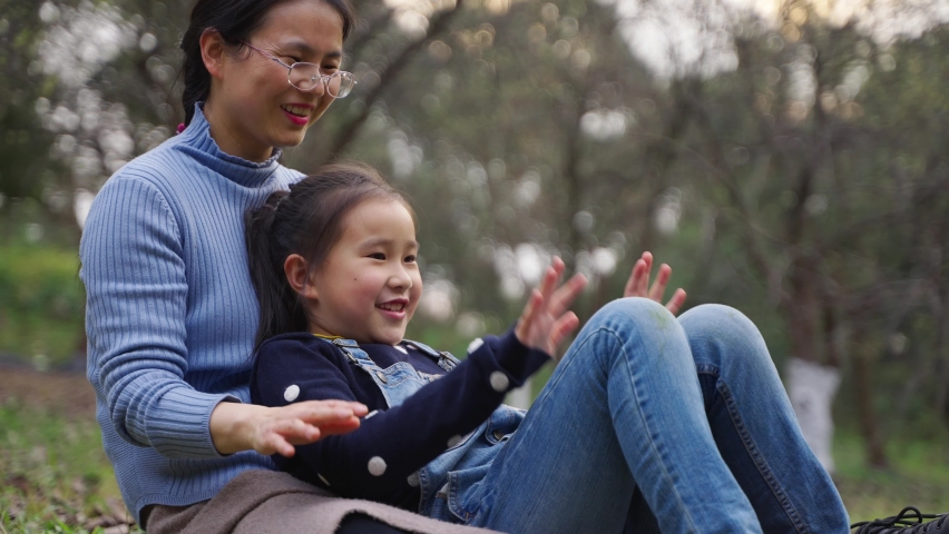 happy asian woman sitting on the ground playing game with her daughgter outdoor in the spring woods