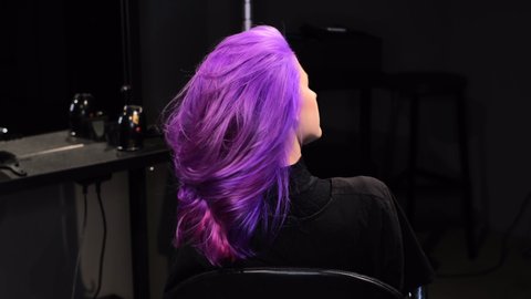 Woman sitting in a beauty salon with pink-purple hair color, curly pretty hair  