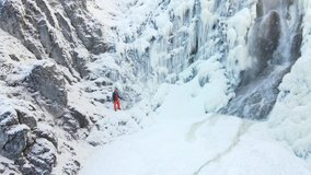 aerial drone shot of hiker with backpack, orange hat and orange pants standing next to waterfall surrounded by icicles and snow in winter - Powered by Shutterstock - Get 15% off with code: PIKWIZARD15