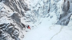 aerial drone shot of hiker with backpack, orange hat and orange pants standing next to waterfall surrounded by icicles and snow in winter. - Powered by Shutterstock - Get 15% off with code: PIKWIZARD15