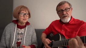 Happy senior couple of retirees sing a song while sitting at home on the couch. A man plays an acoustic guitar - Powered by Shutterstock - Get 15% off with code: PIKWIZARD15