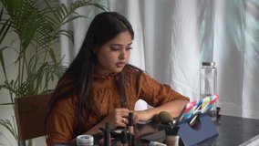 Young Asian woman watching makeup artist tutorial,learning make-up in online class on PC tablet screen.Indian girl learning makeup in online class at home.Video makeup training and blogging concept.
