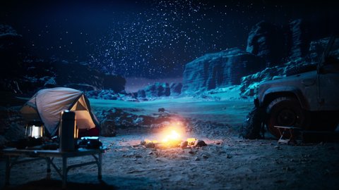 People Camping at Night in the Canyon, Preparing to Sleep in the Tent. Campfire Slowly Burning. Amazing Natural Landscape View with Marvelous Bright Milky Way Stars Shining on Mountains. Zoom in Shot