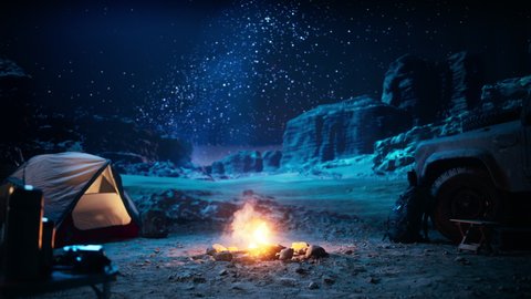 People Camping at Night in the Canyon, Preparing to Sleep in the Tent. Campfire barely Burning, Truck nearby. Amazing Natural Landscape View with Marvelous Bright Milky Way Stars Shining on Mountains