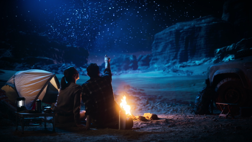 Happy Couple Camping in the Canyon, Sitting Watching Campfire and Starry sky Together, She Rests Her Head on His Shoulder. Two Traveling people On Inspirational Vacation Trip Marvel at Milky Way Stars | Shutterstock HD Video #1067850689