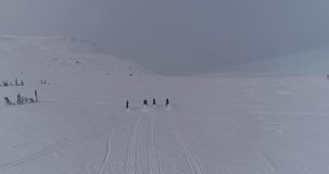 Aerial view: four snow bikers on snowmobiles ride together in a mountain valley. an epic video of a friendly team of snowmobilers riding through a large snow-white canyon high in the mountains at dawn