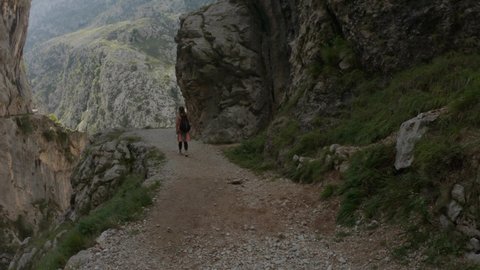 Cain, Spain - September 1, 2020: SLOW - Female hiking trough the Cares Route in the heart of Picos de Europa National Park, Spain. Narrow and impressive canyon between cliffs, bridges and footpaths.
