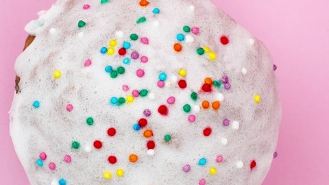 slow motion of easter cupcake with white frosting and multicolored confetti on a pastel pink background homemade holiday close-up. Concept for religious spring break