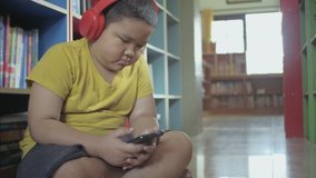 Asian little boy with red headphones using smartphone at home.