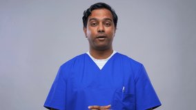 healthcare, medicine and communication concept - indian doctor or male nurse in blue uniform having video conference over grey background
