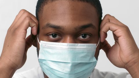 Preventive measures and personal safety. Close up portrait of young african american man putting on protective medical mask, slow motion