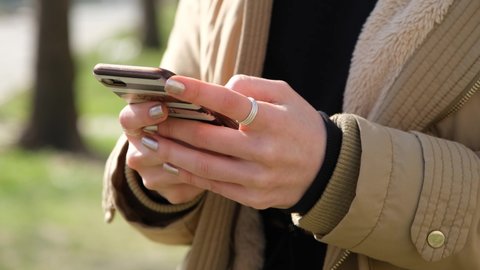A woman in the park is surfing through the news feed on her phone, scrolling through photos, enlarging the picture. Hands close-up. filmed in the park, green grass background