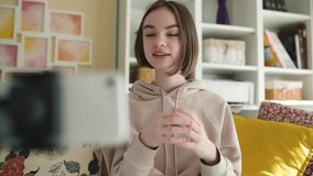 Beautiful teenage girl recording video blog with her smartphone. Young vlogger shooting vlog at home. Teen influencer creating content for her social media account. Social media and blogging concept.