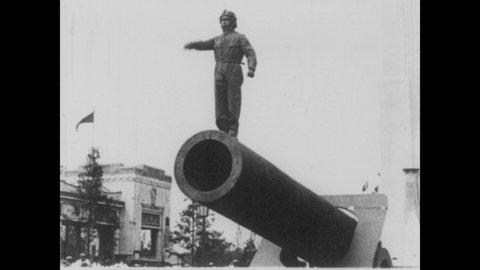 1930s: Man stands atop cannon, climbs into barrel, waves. Cannon barrel tilts up, launches man from within, man falls into net.