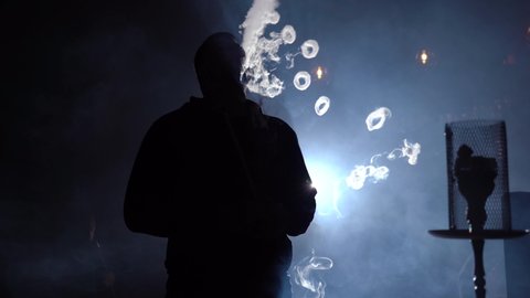 Portrait man smoking traditional hookah pipe and making smoke clouds in form rings. Man exhaling smoke in hookah cafe or lounge bar.