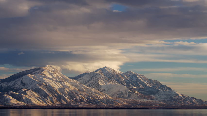 Time lapse over snowcapped mountain range looking at Mt. Nebo from over Utah Lake during sunset.