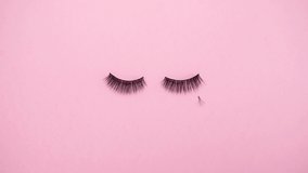 Lashes loss and extension concept. Fake eyelashes fall on trendy pastel pink background. Makeup accessories. Cosmetic products. Top view. Stop motion animation. Beauty pattern. Looping video.