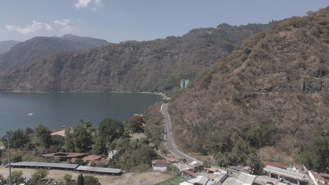Aerial Drone view of a Mountain Road in Panajachel with cars passing by and a boat on Lake Atitlan | mountainous landscape and sunny day