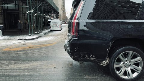NYC, USA - FEB 18, 2021: black Cadillac Escalade SUV driving through snow rain ice sleet and slush in cold winter Manhattan New York City.