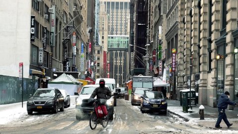 NYC, USA - FEB 18, 2021: Grub Hub delivery man on bicycle riding delivering in K-Town with Korean restaurants and shops on street winter snow Manhattan New York City.