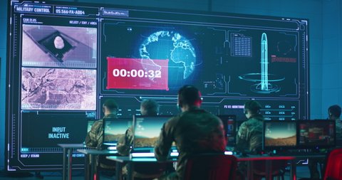 Back view of anonymous soldiers using computers against large screen with count down and online video of nuclear missile launch