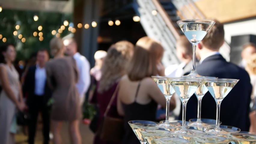 Close-up shooting pyramid of glasses of champagne stands on the buffet table against the backdrop of a cheerful crowd of guests. Royalty-Free Stock Footage #1067882834