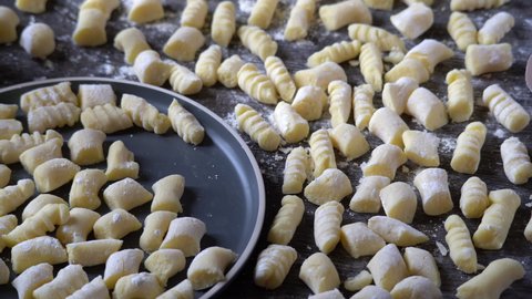 Gnocchi preparation steps: Raw uncooked homemade gluten-free potato gnocchi on a plate and dark table. Sprinkled flour on top. Creating authentic pasta dough for an Italian dish