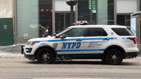 NYC, USA - FEB 18, 2021: NYPD police vehicle driving away in snow on winter day Midtown Manhattan New York City.