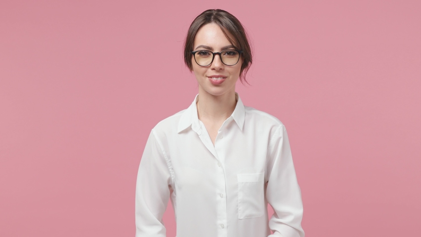 Smiling young business woman in shirt glasses isolated on pink background studio. Achievement career wealth concept. Point index finger on bitcoin coin currency kissing showing thumb up like gesture