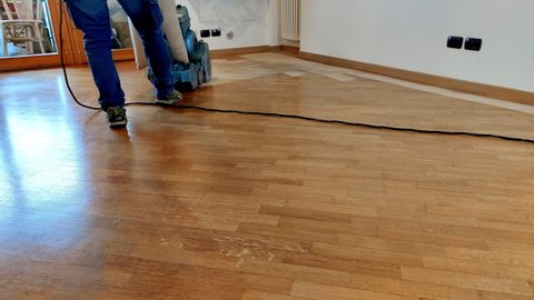 Worker man sanding wooden floor of parquet, with pad sander machine in an empty room during a renovation. Sand and refinish hardwood floors.
