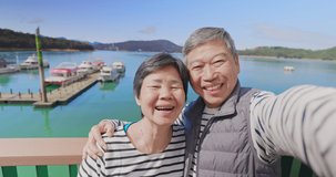 Asian elderly couple have video chat by mobile phone happily outdoor near water