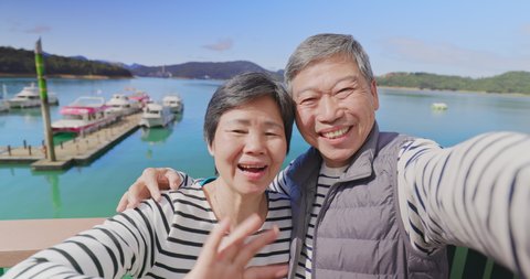 Asian elderly couple have video chat by mobile phone happily outdoor near water