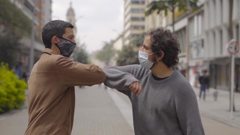 Two friends saying hello with their  elbows to avoid physical contact both are wearing masks to prevent coronavirus in bogota colombia