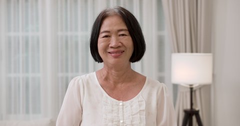 Closeup face portrait of happy and healthy Asian senior elderly gray and black-haired female smiling at camera. The old woman standing in living room with a smile. Happiness of elderly concept.