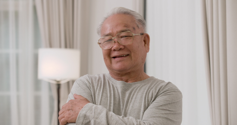 Closeup face portrait of happy Asian senior elderly gray-haired male with glasses smiling at camera and arm crossed. The old man standing in living room. Happiness of elderly concept. | Shutterstock HD Video #1067899121