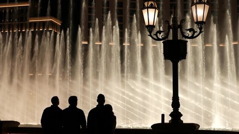 LAS VEGAS, NEVADA USA - 13 DEC 2019: People looking at Bellagio fountain musical performance at night. Contrast silhouettes and glowing dancing splashing water. Entertainment show in gambling city.
