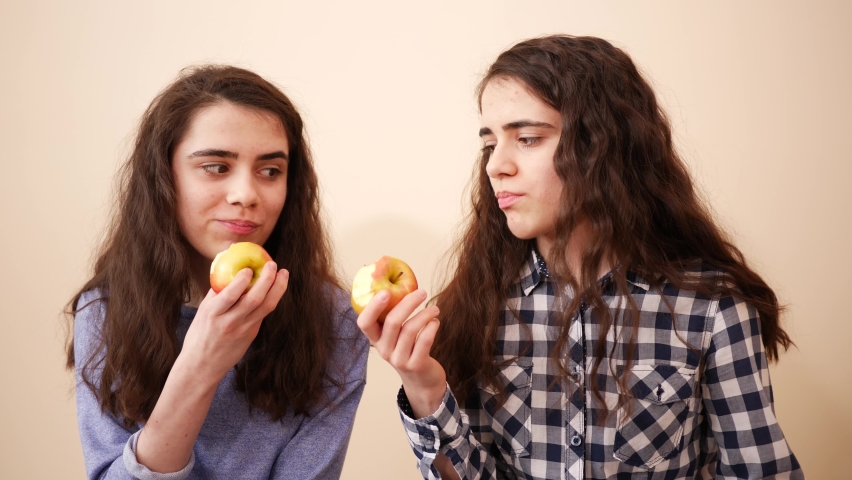 Teenager sisters cute twin girls together have fun eating ripe apples - two kids portrait bite and chew fruits