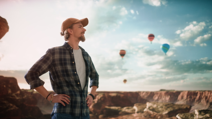 Portrait of a Young Handsome Tourist Sightseeing on Top of a Rocky Canyon Valley. Adventurous Male Backpacker on a Hiking Journey Trip. Hot Air Balloon Festival in Mountain National Park.