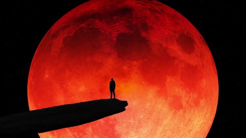 The silhouette of a man standing on a cliff edge watching a giant blood moon in the night sky.