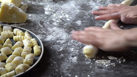 Gnocchi preparation steps: hands shaping gnocchi snake roll. homemade gluten free mashed potato dough roll. Creating fresh Italian pasta on a dark table with flour