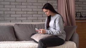 Focused serious young woman using smartphone, communicates in the chat or social media, online shopping, transfers money to charity. Millennial lady spending time at home with cell gadget technology
