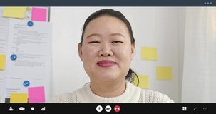 Young Asian woman smiling waving hand and talking on video call in office for mobile job and remote working concepts