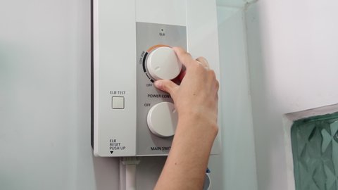A woman turns on the water heater temperature regulator. Water temperature in the electric boiler.