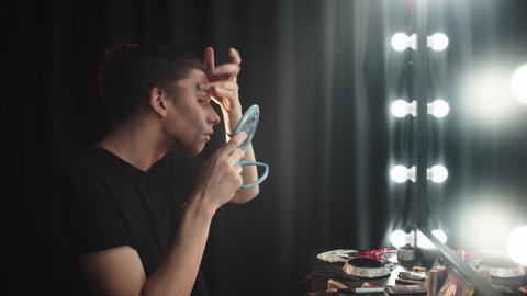 Drag artist - young man doing his eyebrows - checking their dryness and applying te powder on top