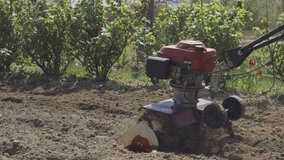 Farmer cultivates the soil in the garden using a tiller - motor cultivator. Man in hat and rubber boots. Footage 4k. Close view