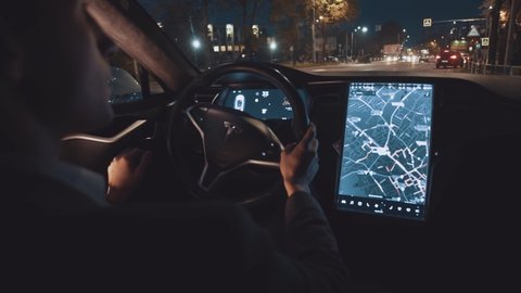 Lviv, Ukraine - August 22, 2020: Tesla driving. In car young confident businessman driving car using map navigation sound assiatant notification app display technology.