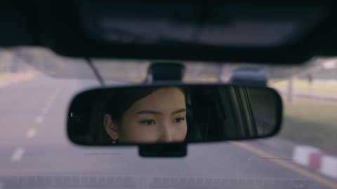 Closeup Asian woman driving a car reflected in rear view mirror on the road