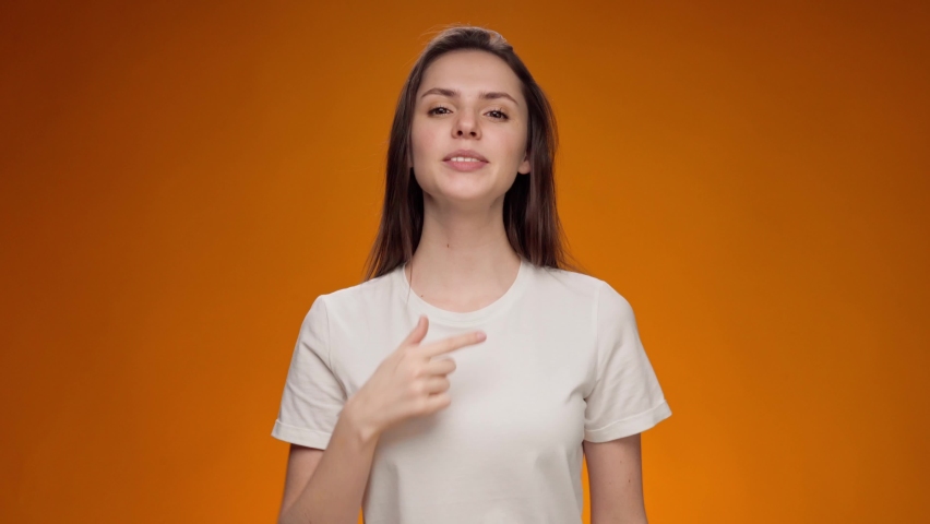 Friendly young woman communicating with deaf-mute sign language against yellow background | Shutterstock HD Video #1067937836