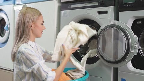 Young blonde puts laundry in the washing machine in the public laundry room. Public self-service laundry.
